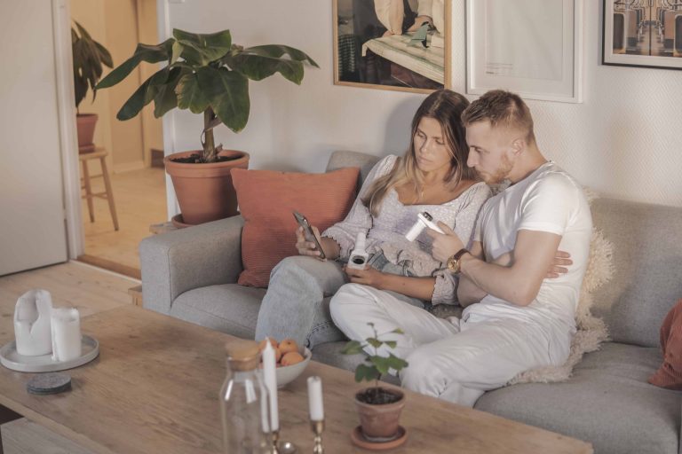 A couple sitting in a couch in their living room with a phone and a spirometer